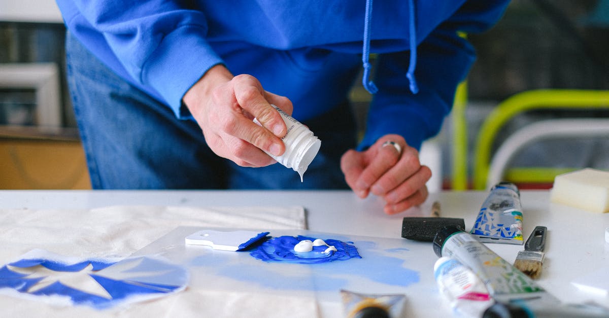 How to add pistachios in a white chocolate mudcake - Unrecognizable male master with small jar adding white paint into blue pigment while working at table with stencil printing in studio on blurred background