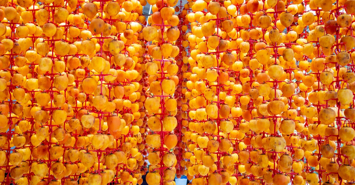 How to avoid having pith on dried orange peels - Colorful whole persimmons with spots on peel hanging on hooks while drying on sunny day outdoors