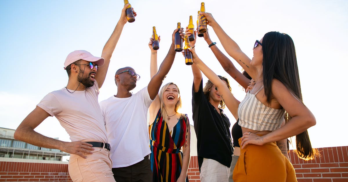 How to chill beer quickly? - Group of cheerful multiethnic friends clinking beer bottles during event on terrace