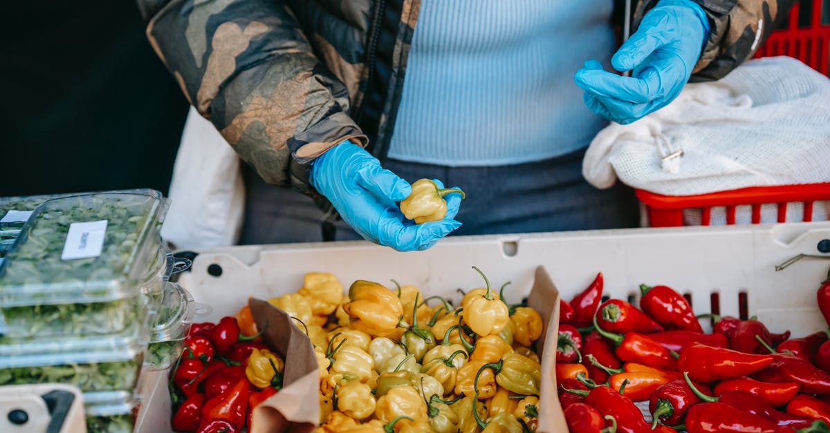 How to choose fresh, ripe (hot) jalapeños? - Crop anonymous person in latex gloves carrying market basket and choosing ripe yellow and red capsicums in vegetable supermarket