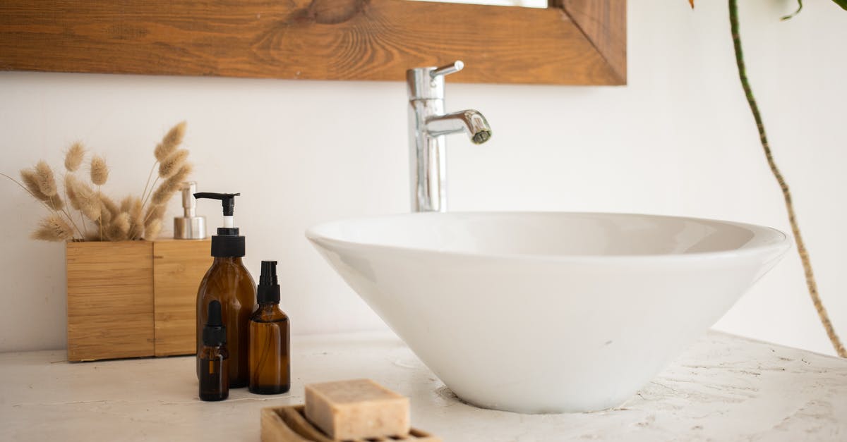 How to clean a cork bottle stopper? - Interior of bathroom table with soap and cosmetic oil placed near white sink and faucet under mirror in wooden frame in modern apartment