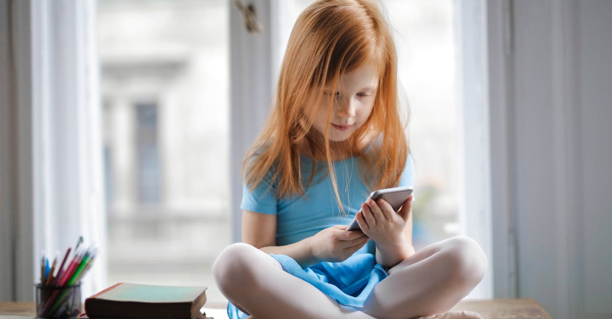 How to clean ginger for tea - Red haired charming schoolgirl in blue dress browsing smartphone while sitting on rustic wooden table with legs crossed beside books against big window at home