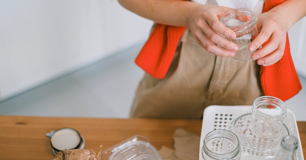 how to clean ginger residue from my plastic juicer containers? - Crop anonymous female in casual clothes standing with glass jar near table while sorting out paper plastic and glass rubbish for recycling