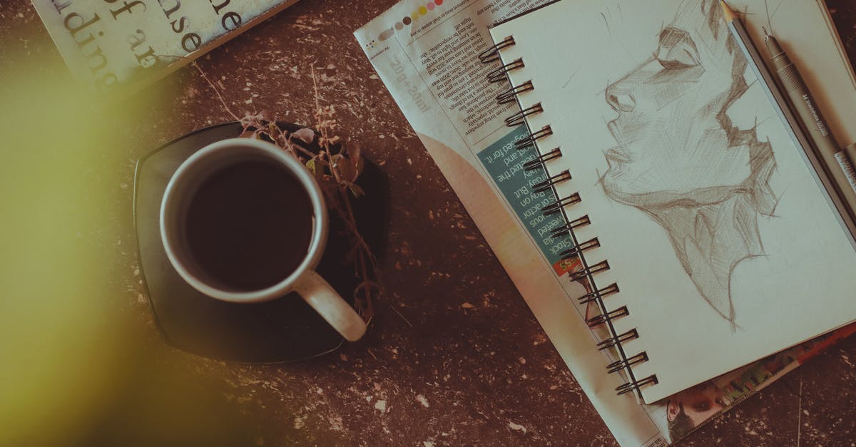 How to clean tea stains from a mug with steel interior? - From above of sketchbook with person portrait near pen and pencil next to mug with drink on saucer with herbs on table near book and newspaper in light room