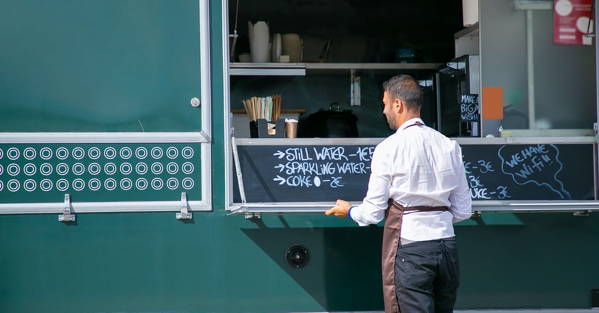 How to cook good "arepas"? - Back view of male seller wearing apron preparing food truck with menu written on board