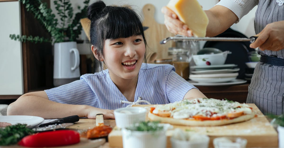 How to cook Parmesan Cheese into a broth without making globs? - Crop anonymous woman grating Parmesan cheese above raw pizza while cooking near cheerful ethnic daughter in kitchen at home