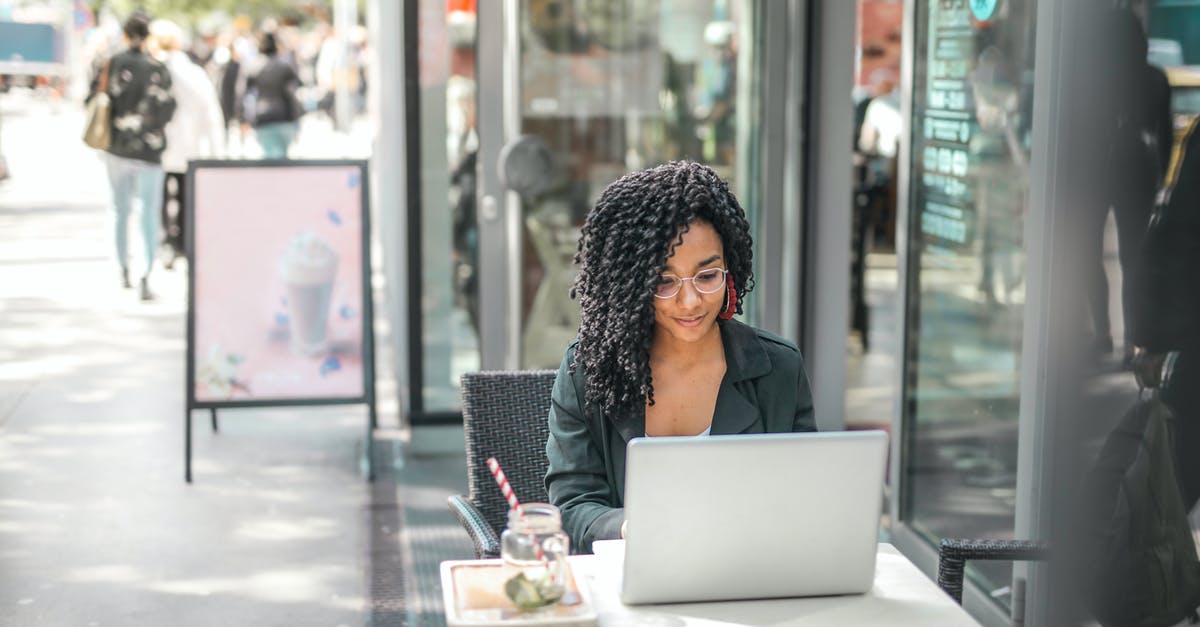 How to correctly use a whisk? - High angle of pensive African American female freelancer in glasses and casual clothes focusing on screen and interacting with netbook while sitting at table with glass of yummy drink on cafe terrace in sunny day