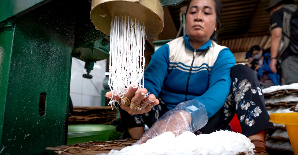 How to create the best veg noodles? - Ethnic lady making noodle on metal machine and wooden covers in factory near people in Vietnam