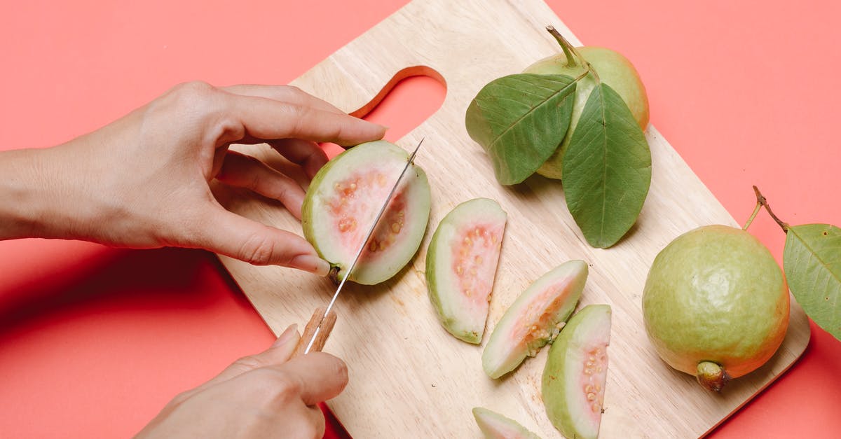 How to deseed a guava? - From above crop anonymous female with knife cutting fresh ripe fruits of guava on wooden chopping board on pink background