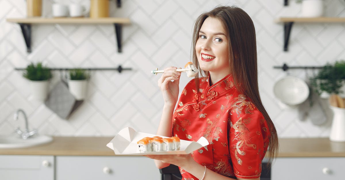 How to dress sushi to better enhance all its flavours? - Happy young female with long dark hair in vivid dress enjoying Japanese traditional cuisine and eating appetizing sushi while having lunch in modern light kitchen
