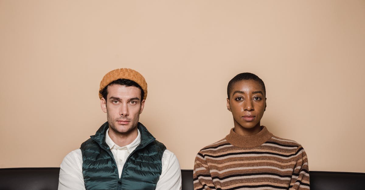 How to efficiently separate bad from good pomegranate arils? - Emotionless multiethnic couple sitting on couch against beige background and looking at camera