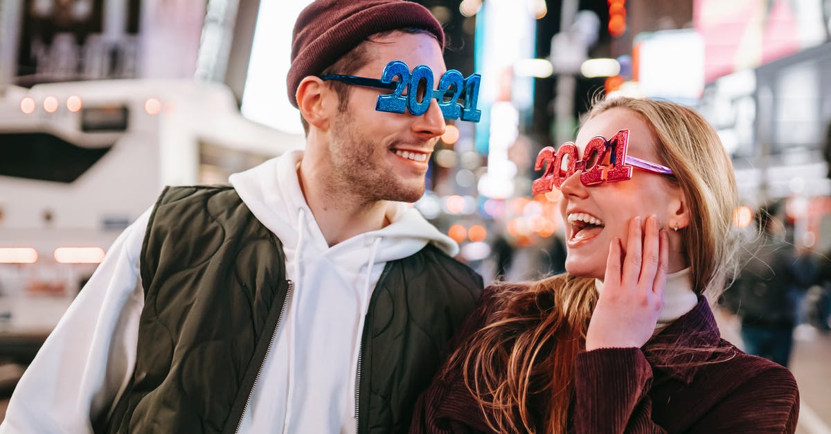 How to evenly spread butter in each square of a waffle? - Smiling couple wearing decorated 2021 glasses looking at each other while standing on street with illuminated buildings on blurred background