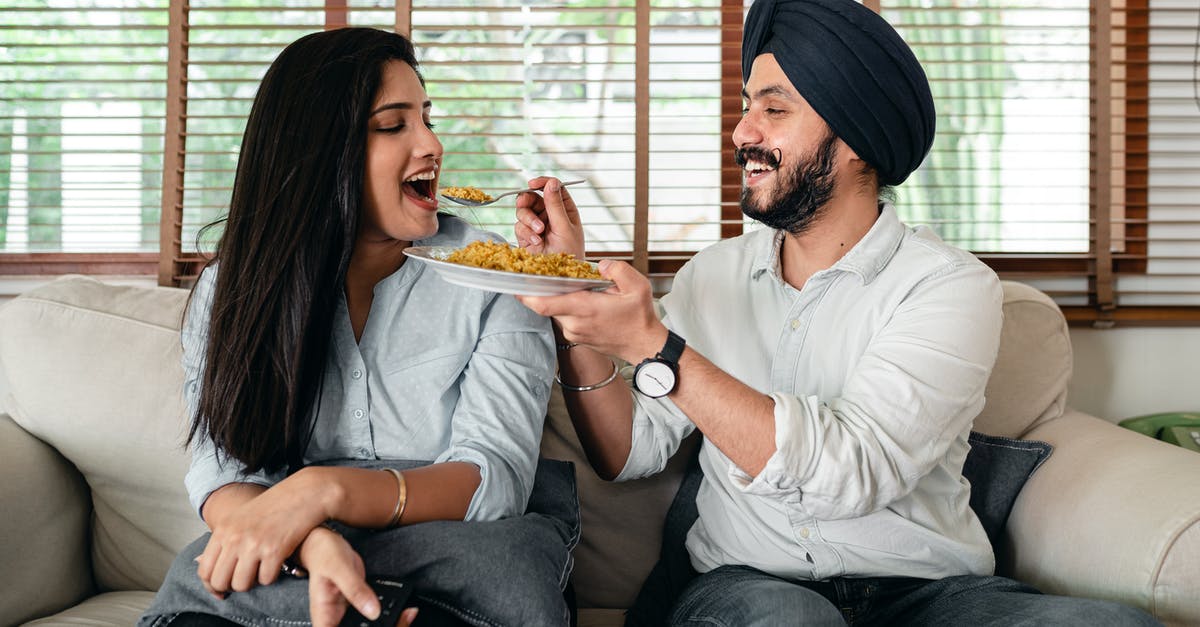 How to Feed a Sour Culture - Delighted ethnic couple having meal on sofa in living room