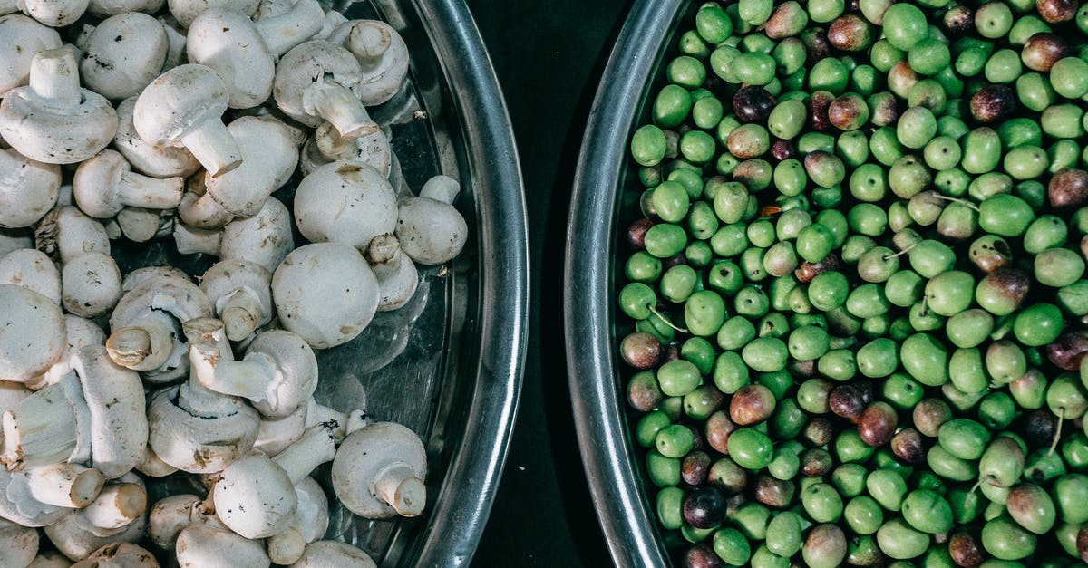 How to get fresh green peas? - Top view composition of ripe raw green peas and fresh mushrooms heaped in steel bowls and placed on dark table