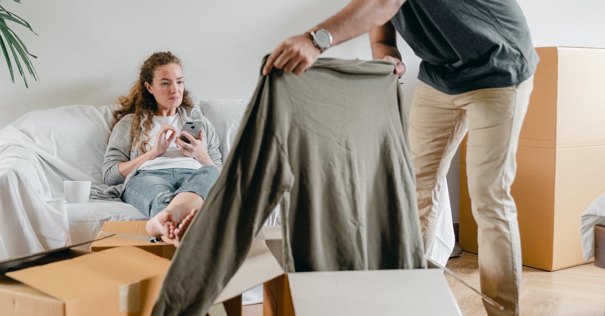 How to get Palm Oil? - Crop anonymous male in watch getting polo neck out of cardboard box while standing near pensive barefoot girlfriend sitting with crossed legs on comfortable couch after moving into new flat