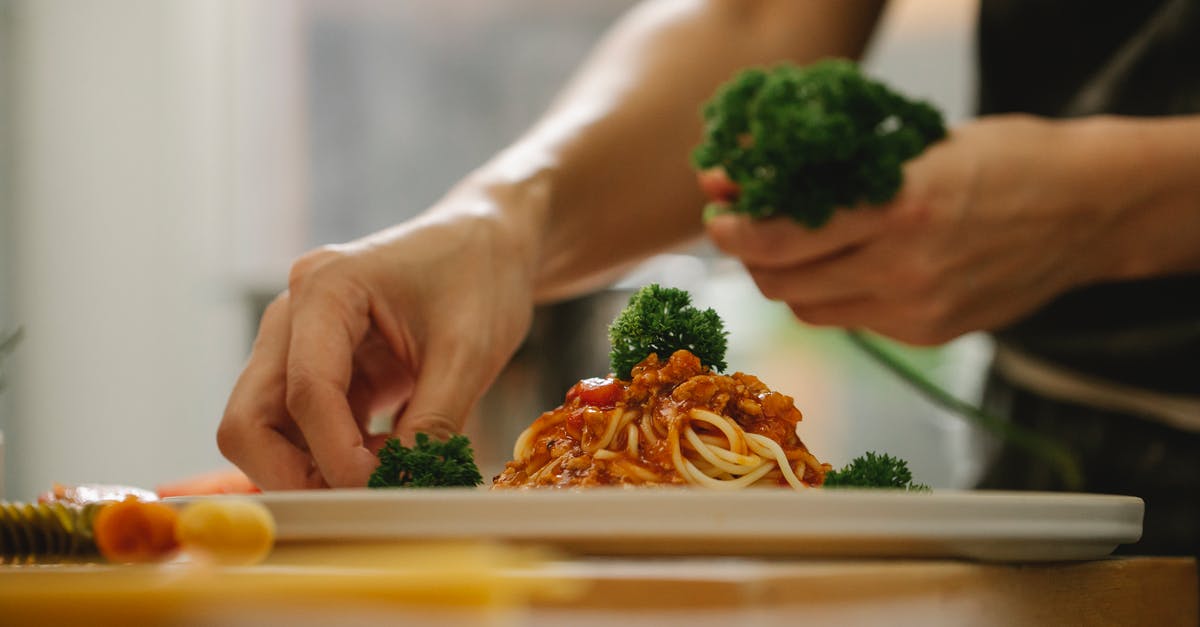 How to get rid of Garlic taste in tomato sauce - Crop anonymous housewife adding ripe parsley on delicious spaghetti with tomato sauce while cooking in kitchen