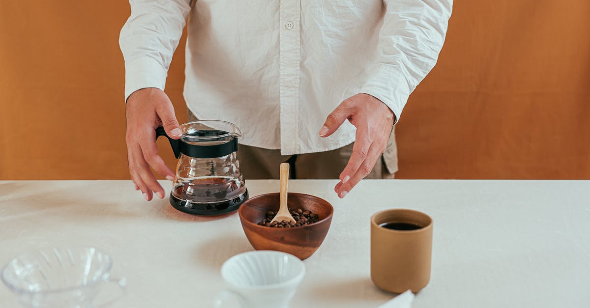 How to hand-select the perfect coffee bean? - Person in White Long Sleeve Shirt Holding Stainless Steel Container With Brown Liquid