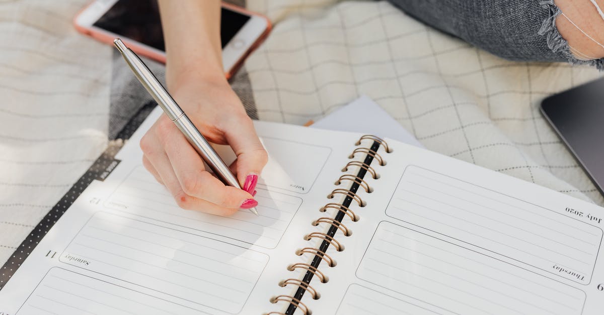 How to have a weekly baking sourdough starter plan - Crop faceless lady in jeans writing in notebook with mobile phone beside while sitting on picnic blanket on sunny day in park