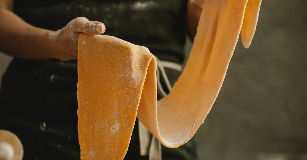 How to keep edible cookie dough soft after refrigerated? - Crop anonymous cook demonstrating soft thin sheet of pasta dough with flour on gray background