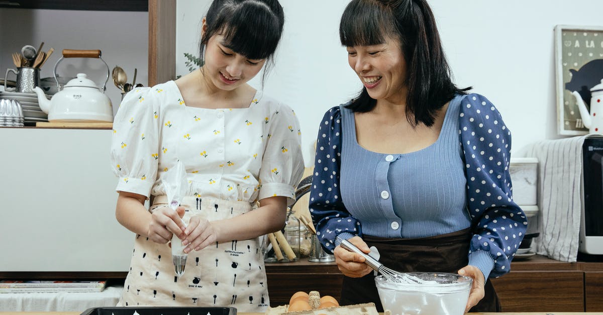 How to know when meringue has been over-whipped? - Happy middle aged Asian female in casual clothes with teenage daughter smiling while preparing tasty meringue cookies in kitchen