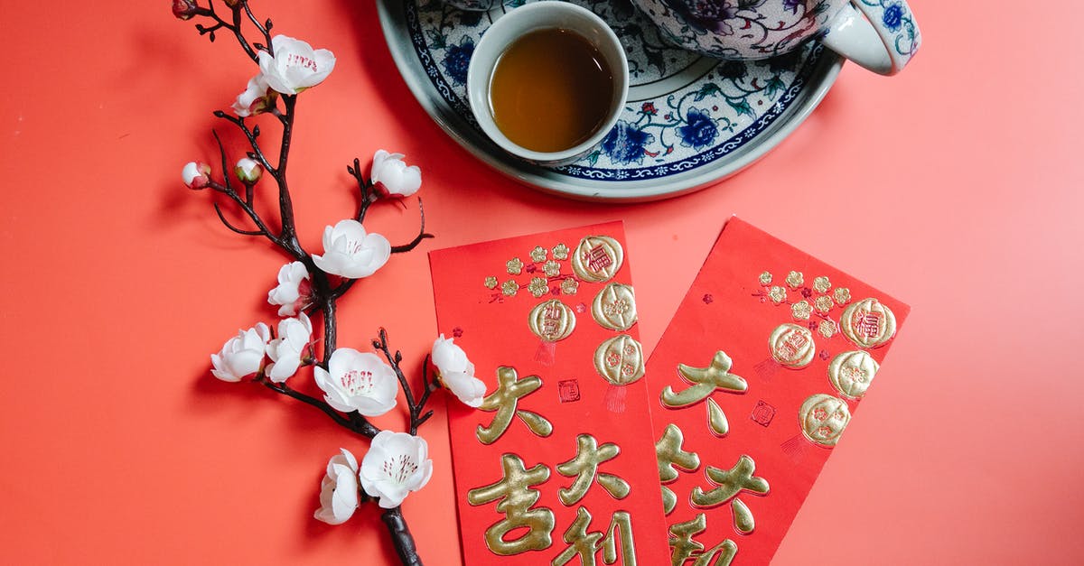 How to make a brewed tea at work? - Top view of oriental packets with hieroglyphs against blossoming flower sprig and tea set during New Year holiday on red background