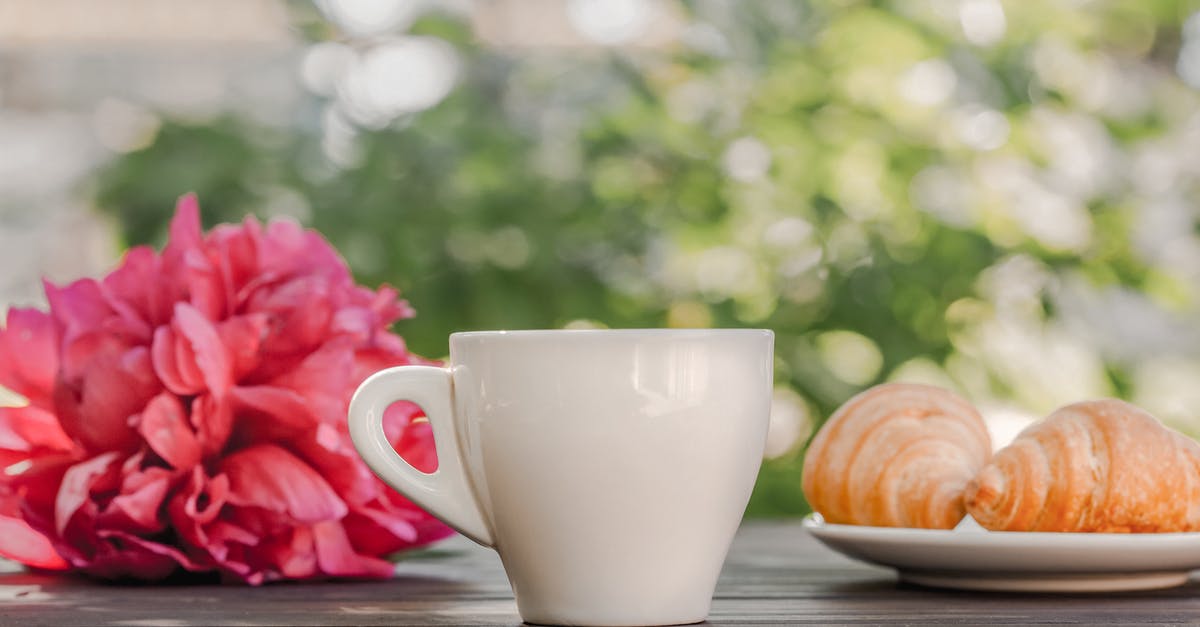 How to make a dessert with dynamically opening flower petals? - Coffee cup with croissants served on table near peonies in green garden in sunlight