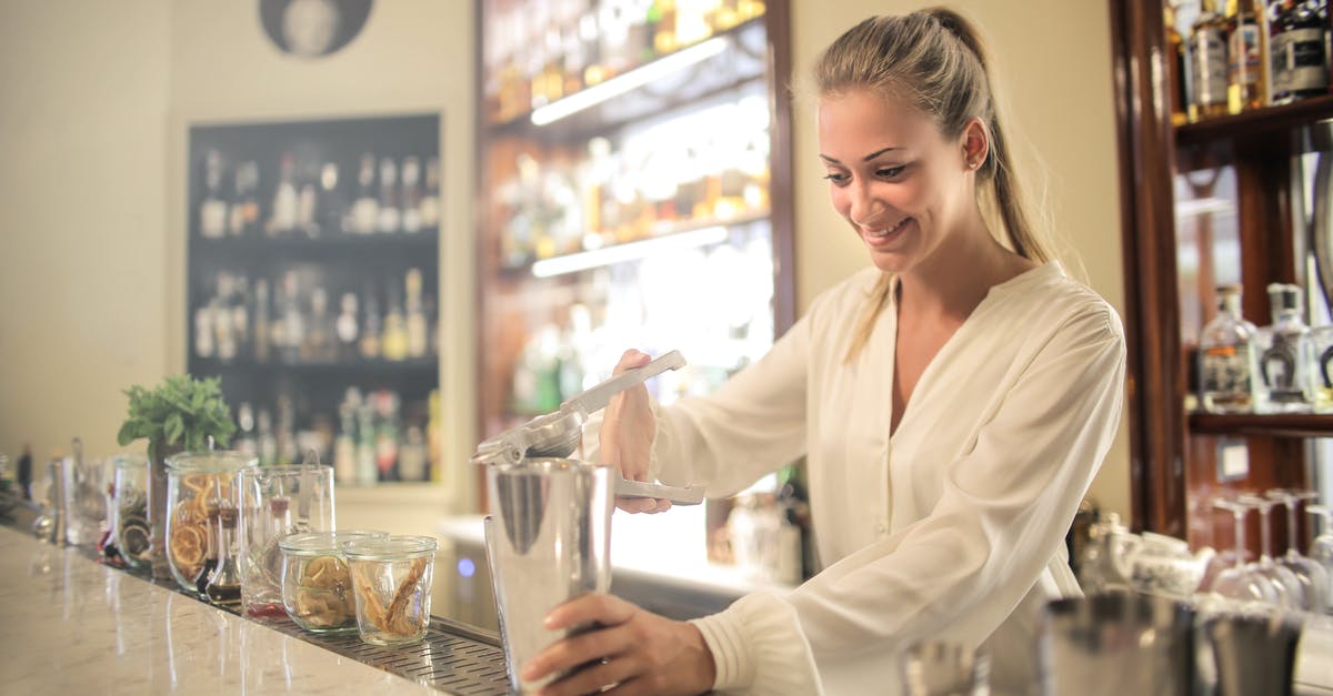 How to make Banana juice - Smiling blonde in white blouse squeezing fresh juice into stainless shaker while preparing cocktail in bar