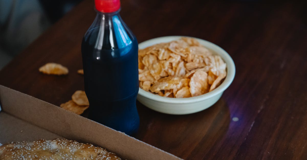 How to make crispy/dry potato chips/crisps? - From above of plastic bottle of soft drink between takeaway pizza with sesame seeds and crispy potato chips at home