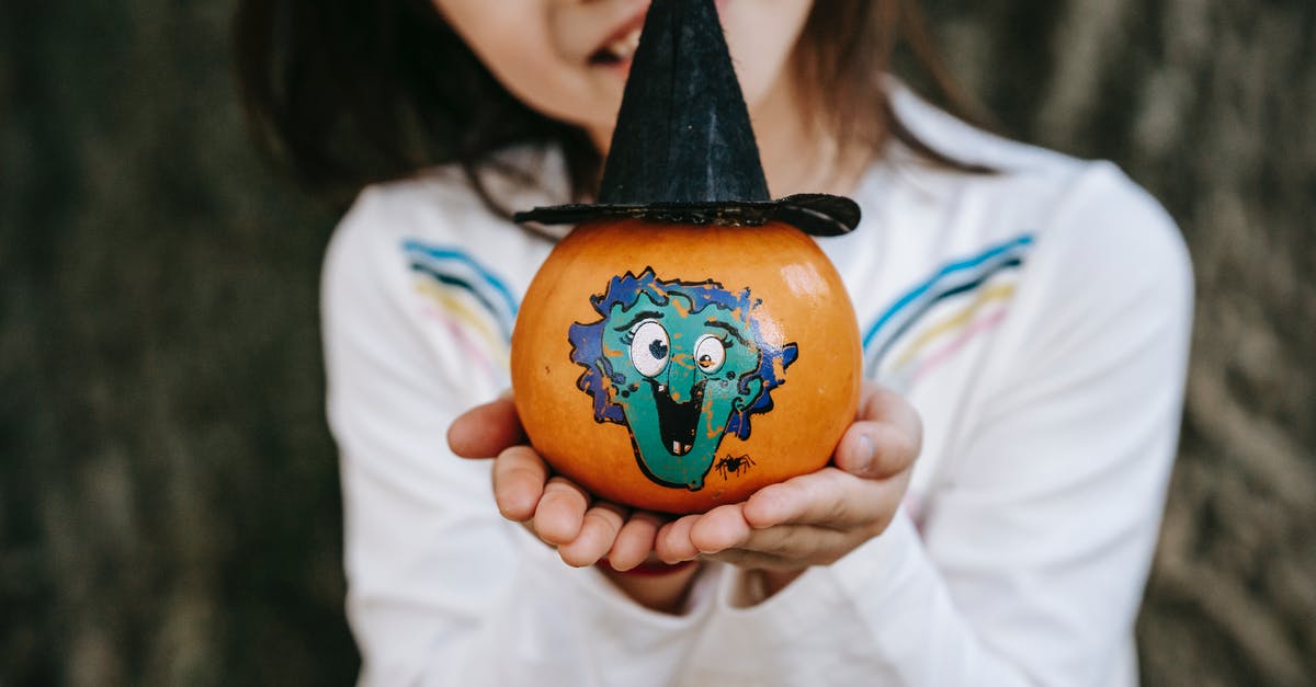 How to make pumpkin extract - Crop little girl in white dress showing colorful pumpkin painted for Halloween and decorated with paper hat