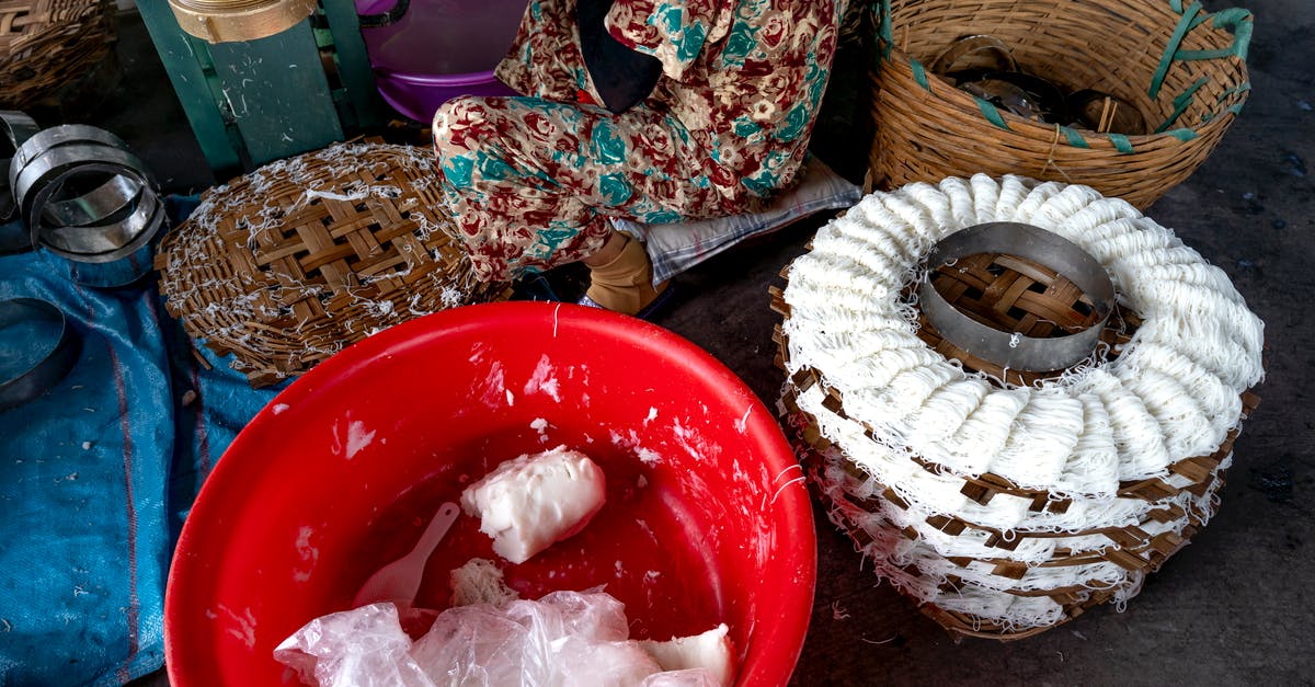 How to make round popcorn? - From above of tool for production of traditional Vietnamese noodles with white dough near plastic container and wicker basket