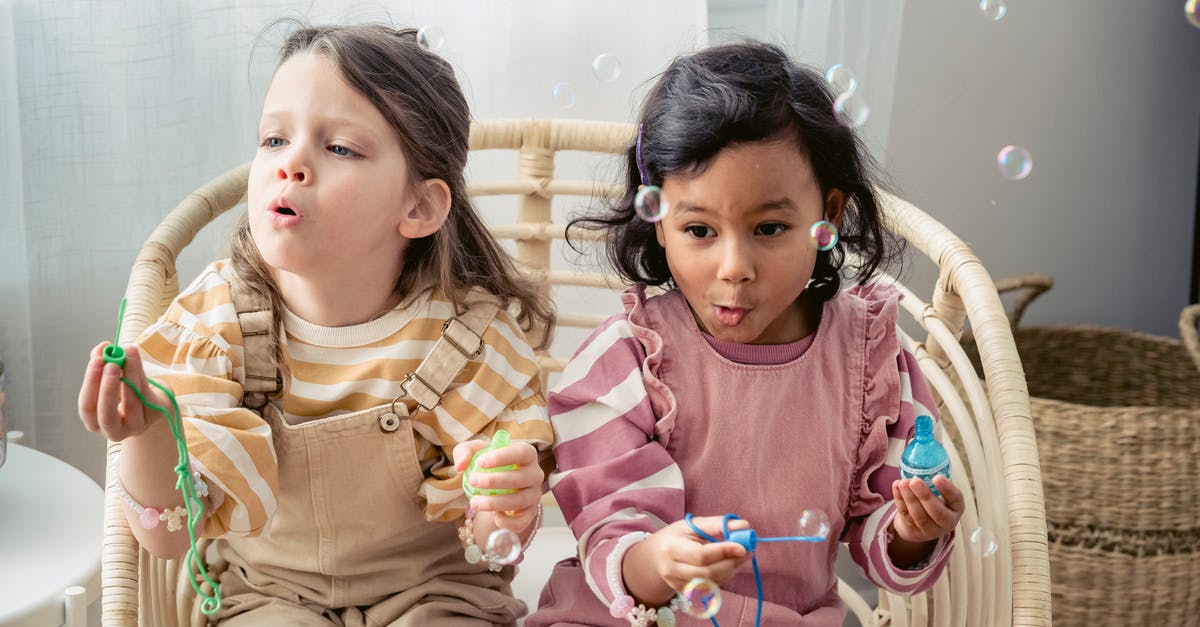 How to make spaghetti stick together? - Carefree multiracial girls blowing soap bubbles in armchair at home