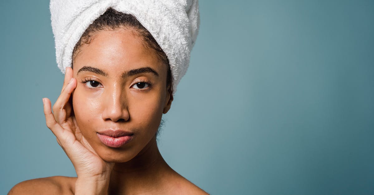 How to Make the perfect French Custard? - Tranquil young black female with pure skin and white towel on head touching face and looking at camera after spa procedures against blue background