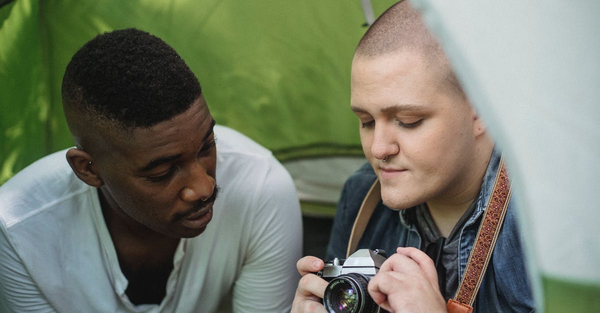 How to make use of old apples? - Young male showing sharing retro photo camera with African American friend while sitting in green tent