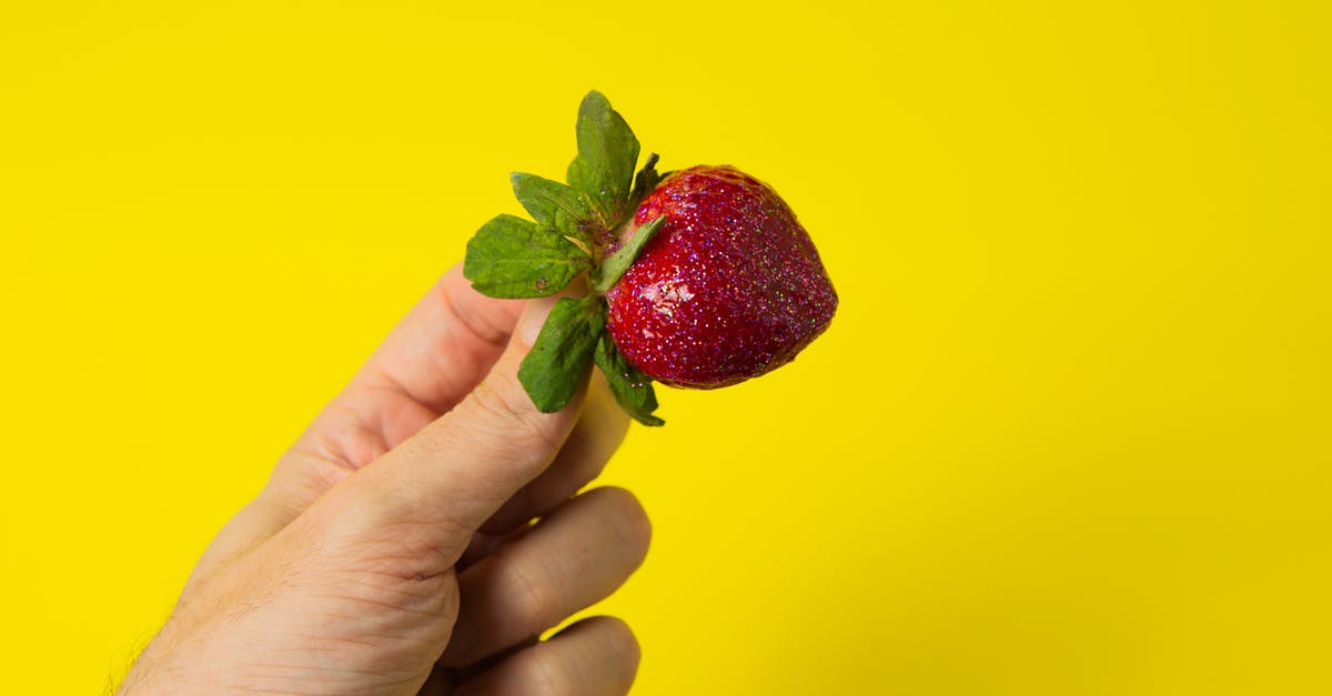 How to make vivid color candy with a small quantity of natural food coloring? - Crop unrecognizable person demonstrating fresh ripe yummy strawberry with green leaves on bright yellow background