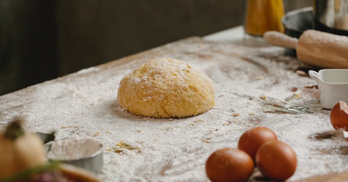 How to make wafer balls - From above of raw dough placed on table covered with flour near kitchen utensils and eggs in kitchen with ingredients