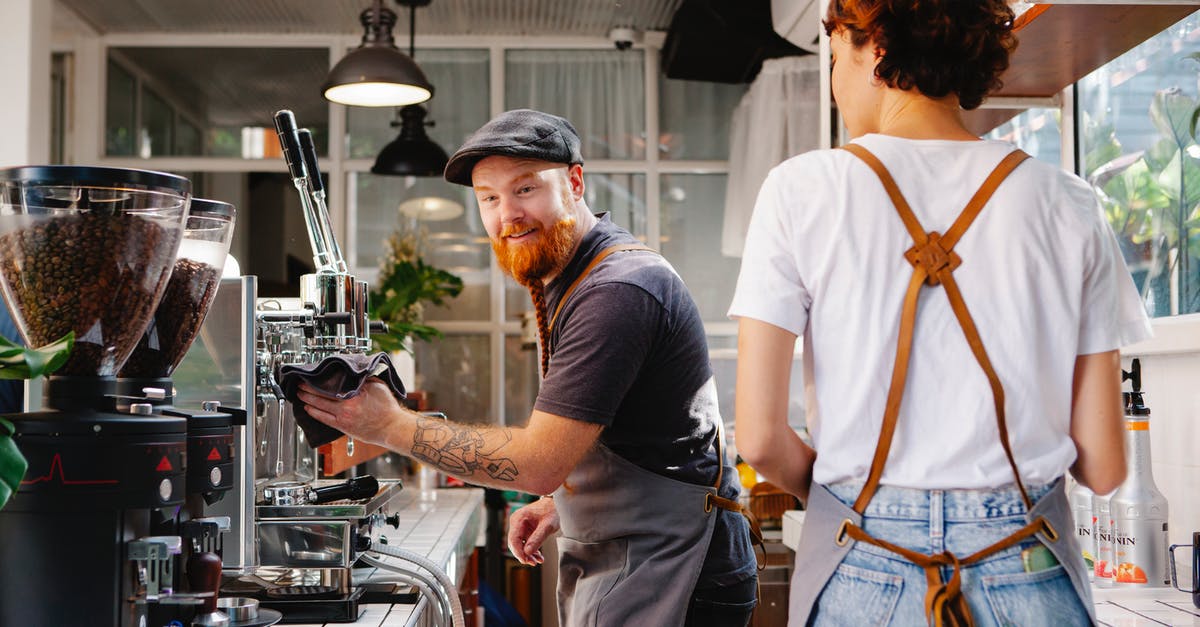 How to make whole bean blonde Starbucks without machine - Cheerful bearded male cafe employee talking to anonymous female colleague against professional coffee maker and grinders