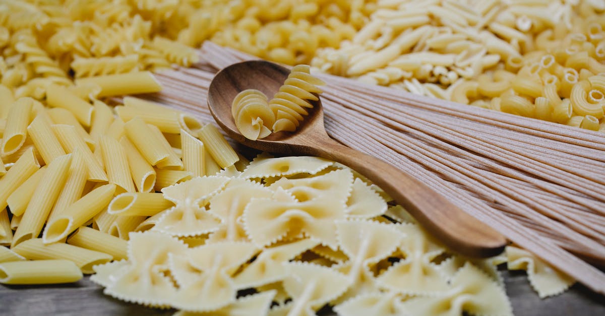 How to mix a spaghetti carbonara? - Arrangement of uncooked various pasta including spaghetti fusilli farfalle and penne heaped on table with wooden spoon