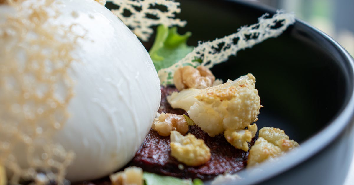 How to mix butter with meat - Closeup of tasty salad with golden cauliflower pieces on toasted meat slices and lettuce leaves with big ball of fresh mozzarella cheese decorated with edible grid in bowl