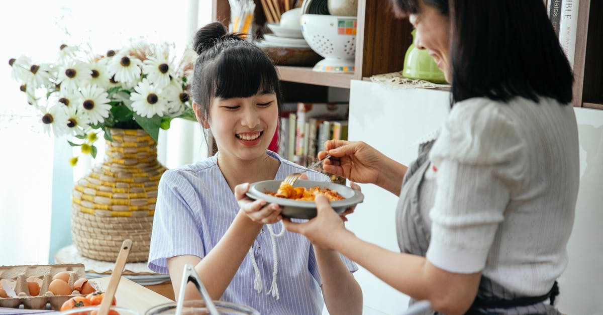 How to mix pasta and sauce evenly? - Delighted Asian female housewives in aprons mixing pasta with sauce in plate while cooking together in kitchen