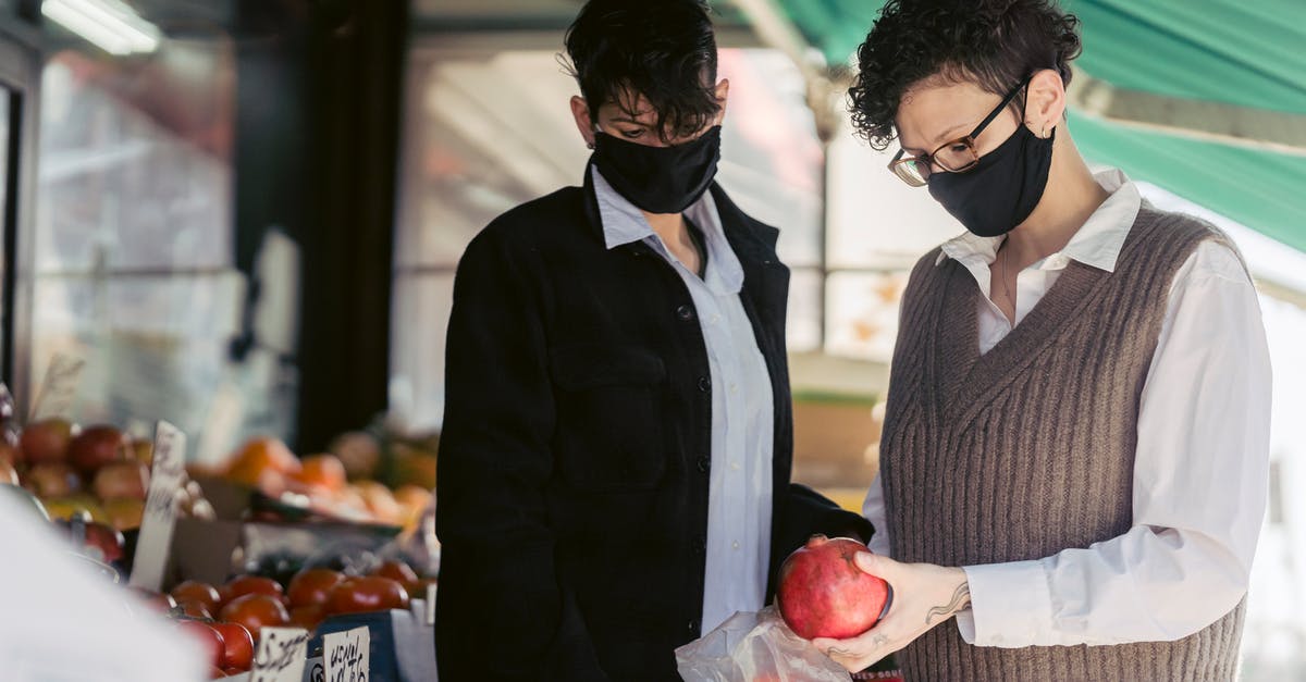 How to not buy the bad apple? - Concentrated young female friends in casual clothes and medical masks choosing fruits in local street food market on sunny day during coronavirus pandemic