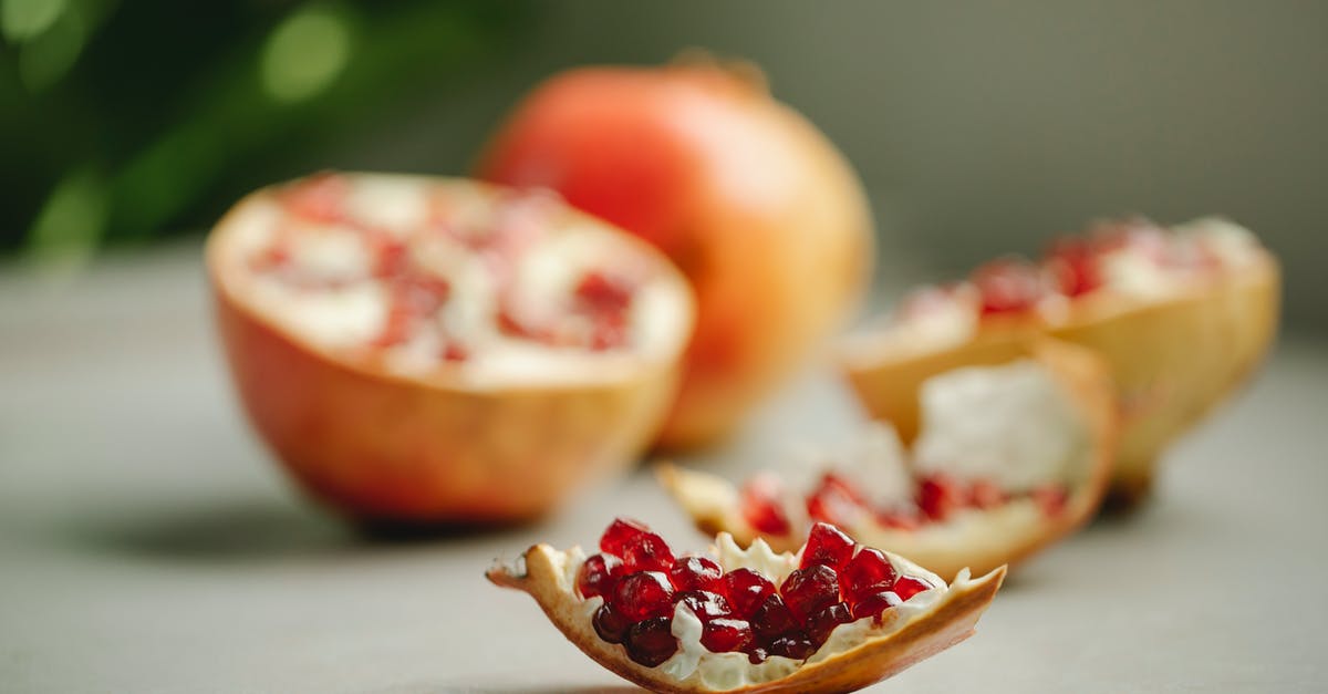 how to peel a pomegranate efficiently? - Chunk of ripe pomegranate with red seeds placed on surface near halves of tasty fruit on blurred background in kitchen