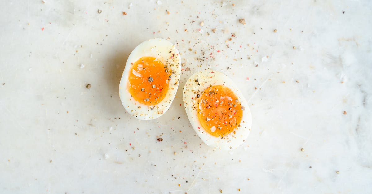How to peel hard boiled eggs easily? - Top view of halved soft boiled egg placed on marble table and spiced with salt and pepper