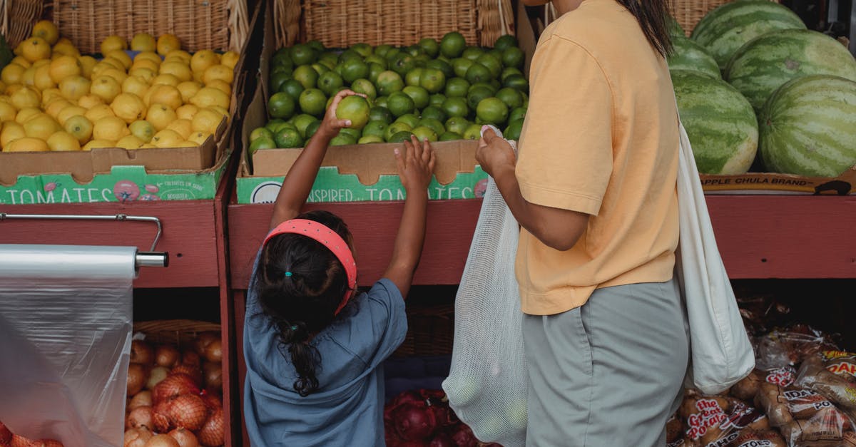 How to pick a good mango at a local store? - Ethnic girl choosing fruit from box in bazaar with mother