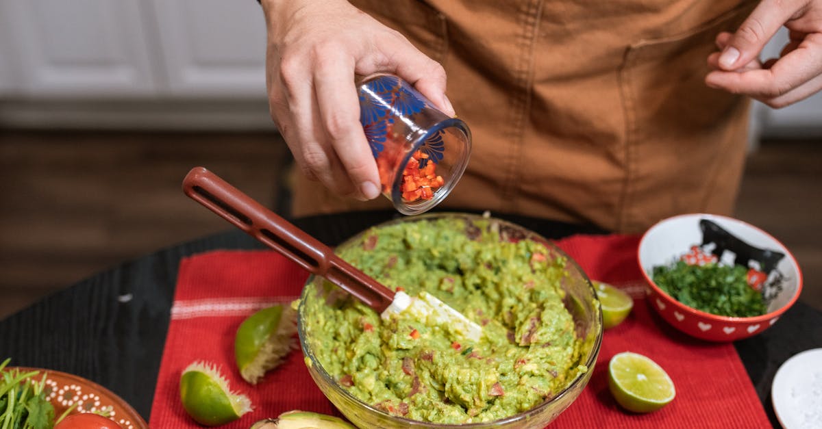How to prepare celery for dipping? - Crop faceless person adding cut tomatoes in bowl with guacamole