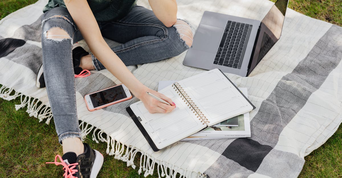 How to prepare shallot greens? - From above crop anonymous female student in casual outfit writing in planner while sitting on warm blanket with smartphone and laptop on green park lawn