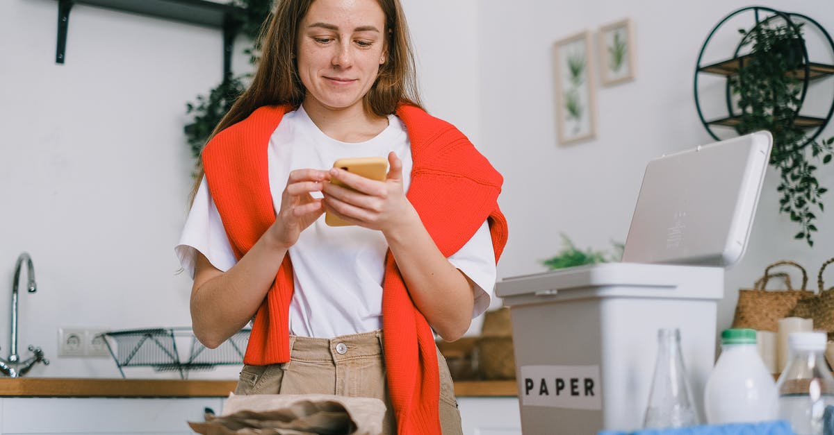 How to preserve and ship home made mayonnaise - Cheerful female browsing mobile phone and standing at table with sorted paper and plastic waste