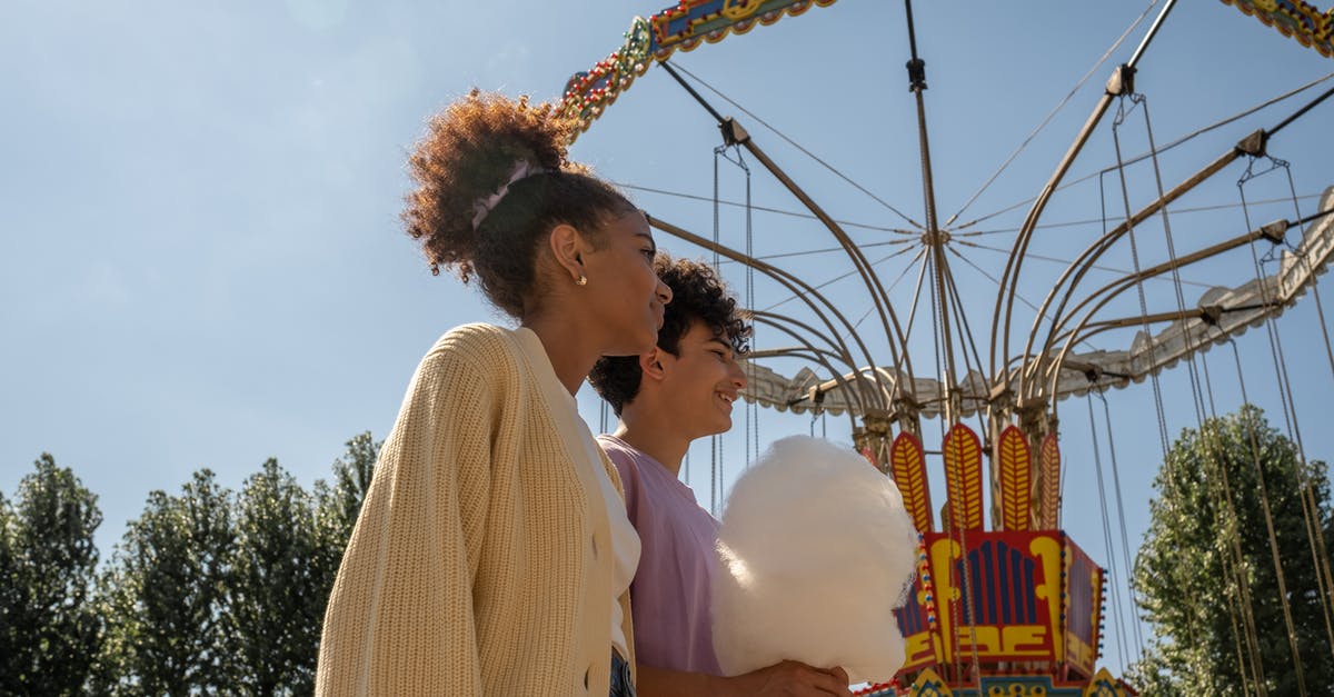 How to preserve cotton candy - Teenage couple walking by big carousel and boy holding cotton candy