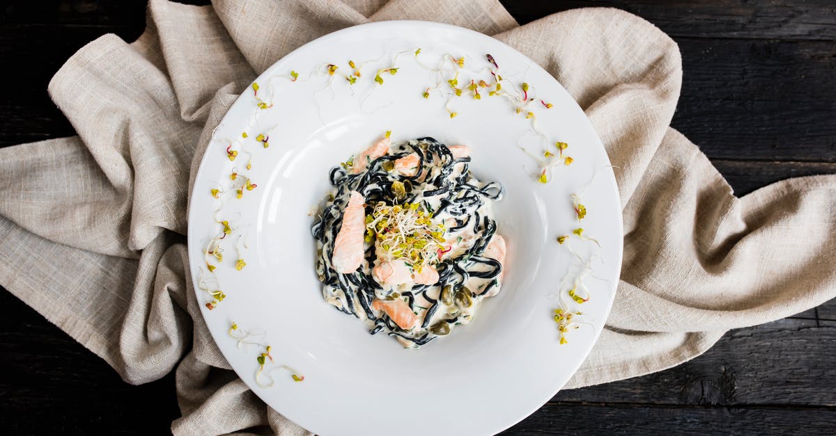 How to prevent creamy sauces from separating upon reheating? - Top view of tasty black spaghetti with cooked red fish slices and sauce in plate with seed sprouts on fabric