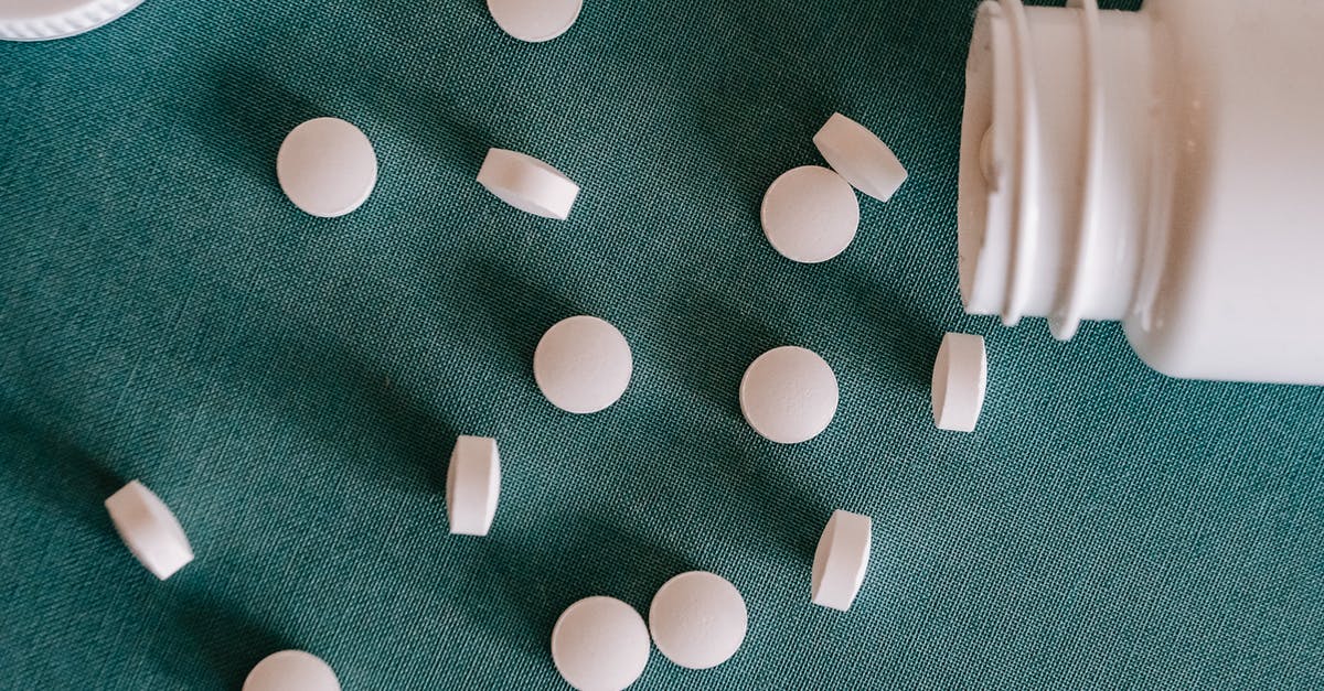 How to prevent liquids from spilling when pouring from measuring cup? - Top view of similar small round white pills spilled from plastic container on green surface