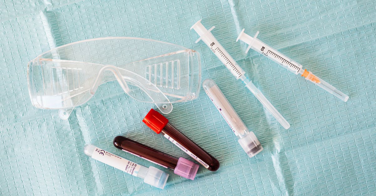 How to prevent liquids from spilling when pouring from measuring cup? - Top view of empty and full of blood vials and plastic syringes and eyeglasses  placed on medical diaper